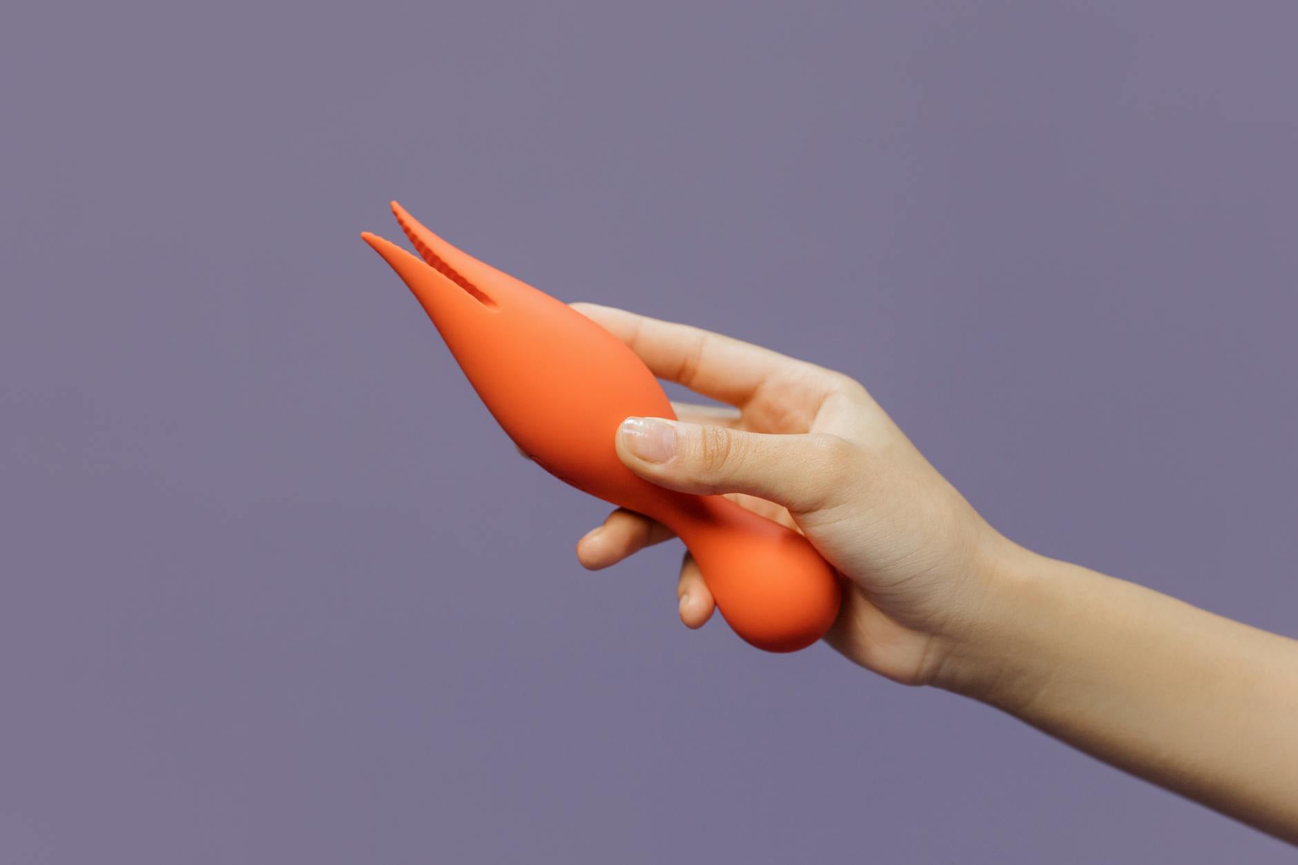 Close-up of a hand holding a modern suction vibrator against a minimalistic purple backdrop