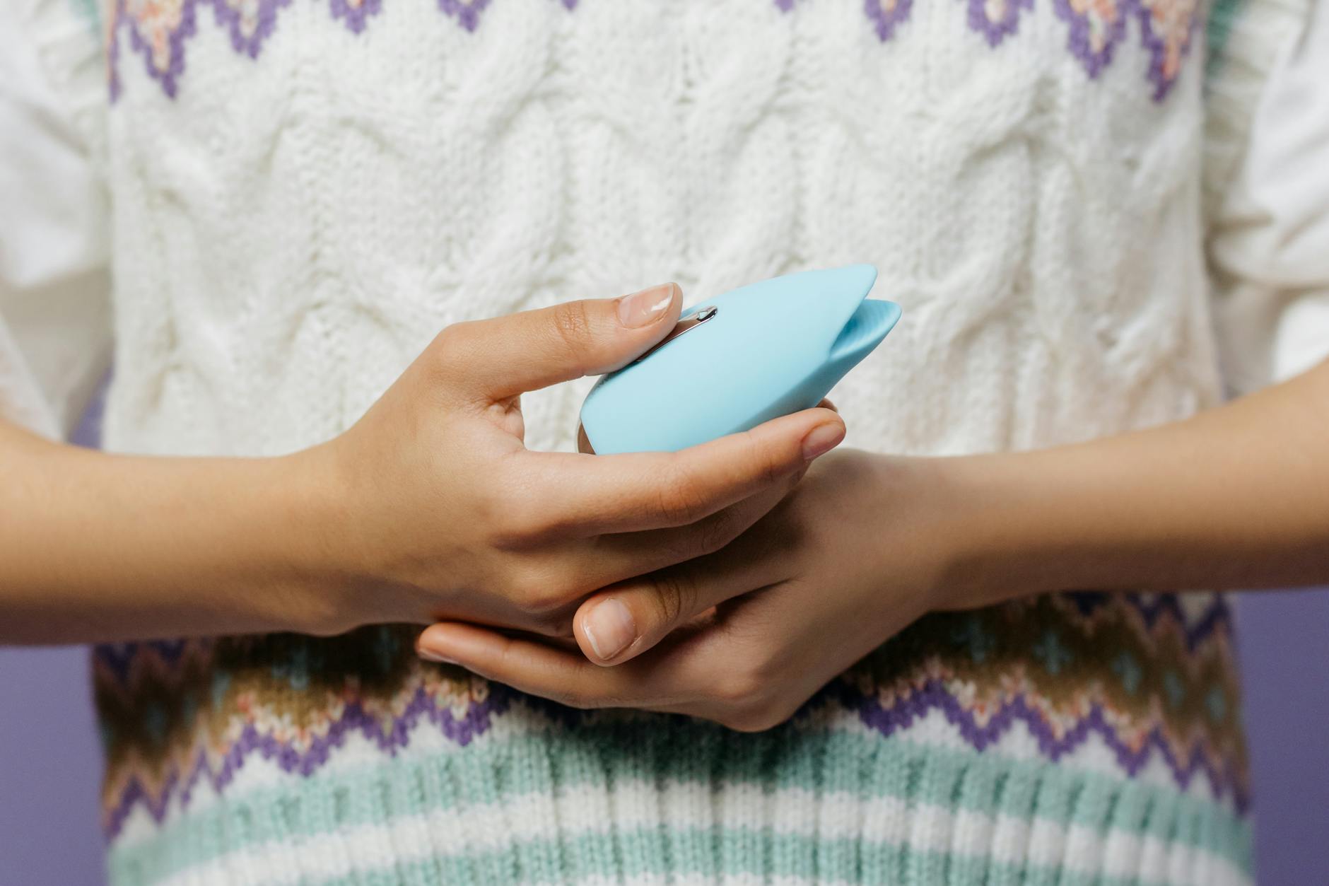 Close-up of hands holding a personal vibrator against a knitted sweater.